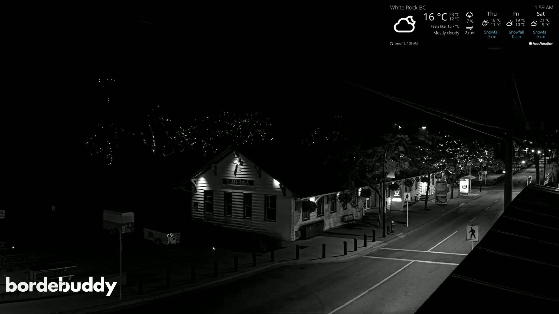 A mostly cloudy night scene shows a street with a building lit up, string lights in trees, and minimal traffic.