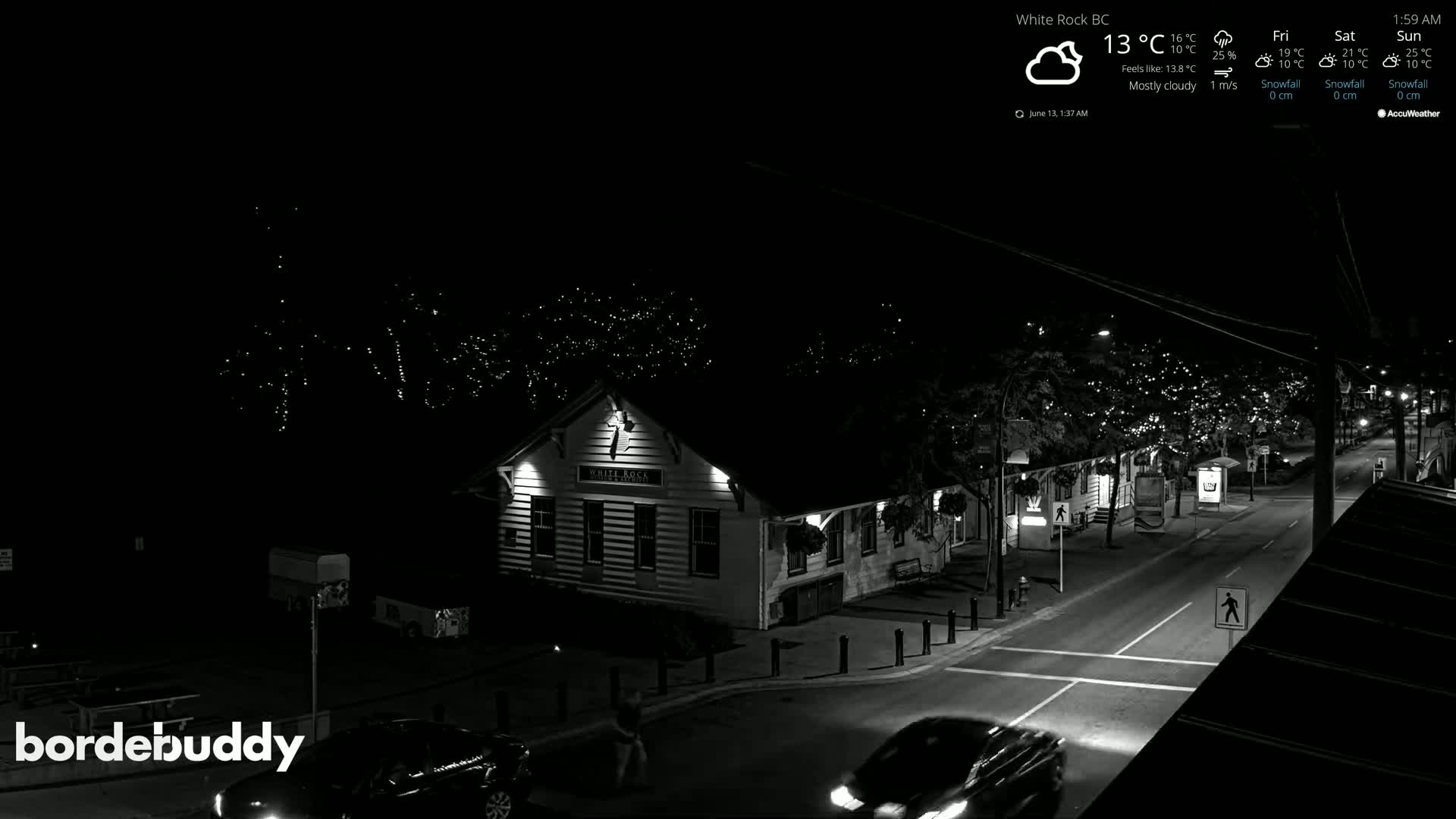 A mostly cloudy night scene shows a street with cars, string lights on trees, and a building illuminated.