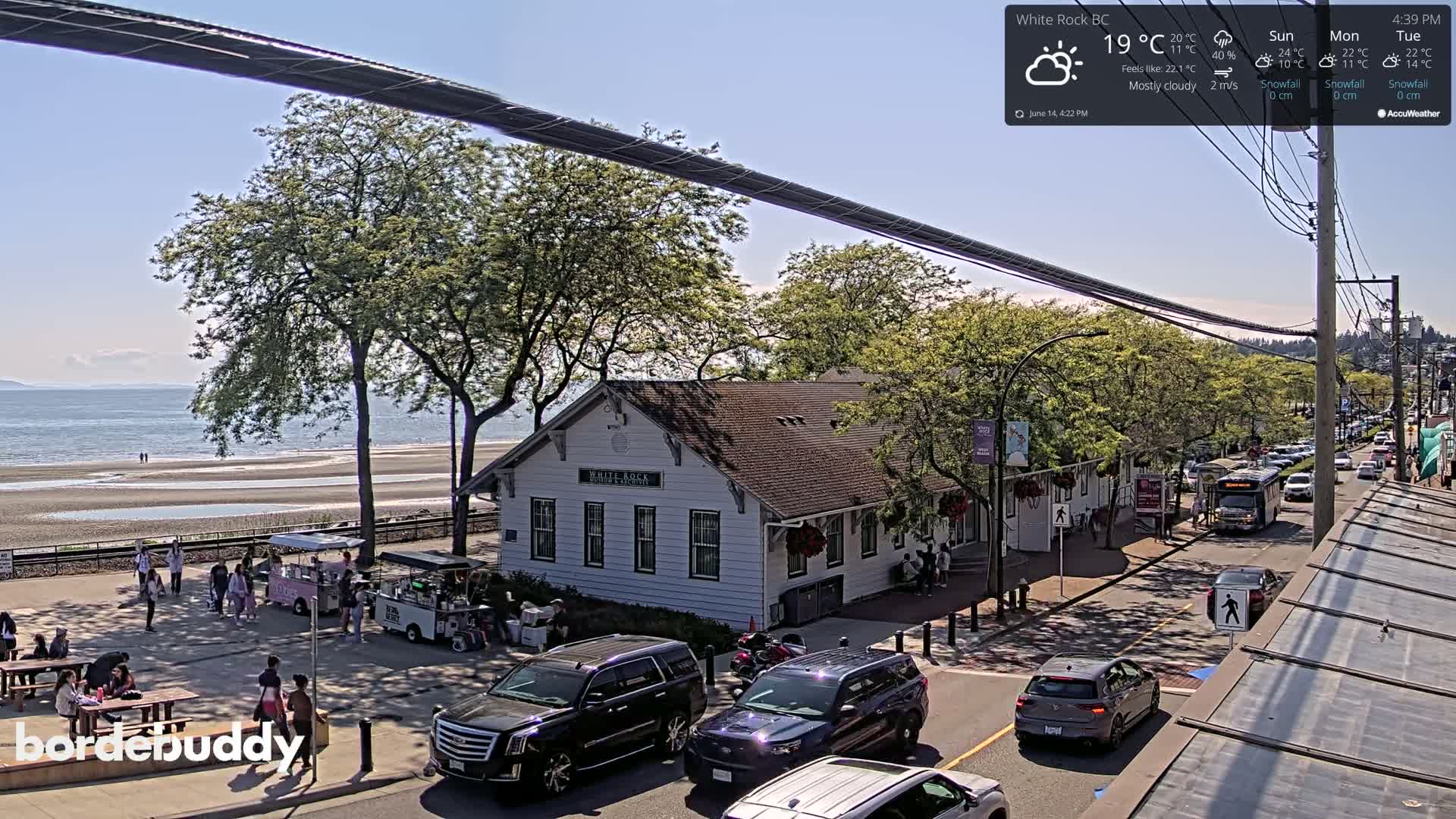 A cloudy day overlooks a seaside town with a white building near a beach and a street with parked cars.