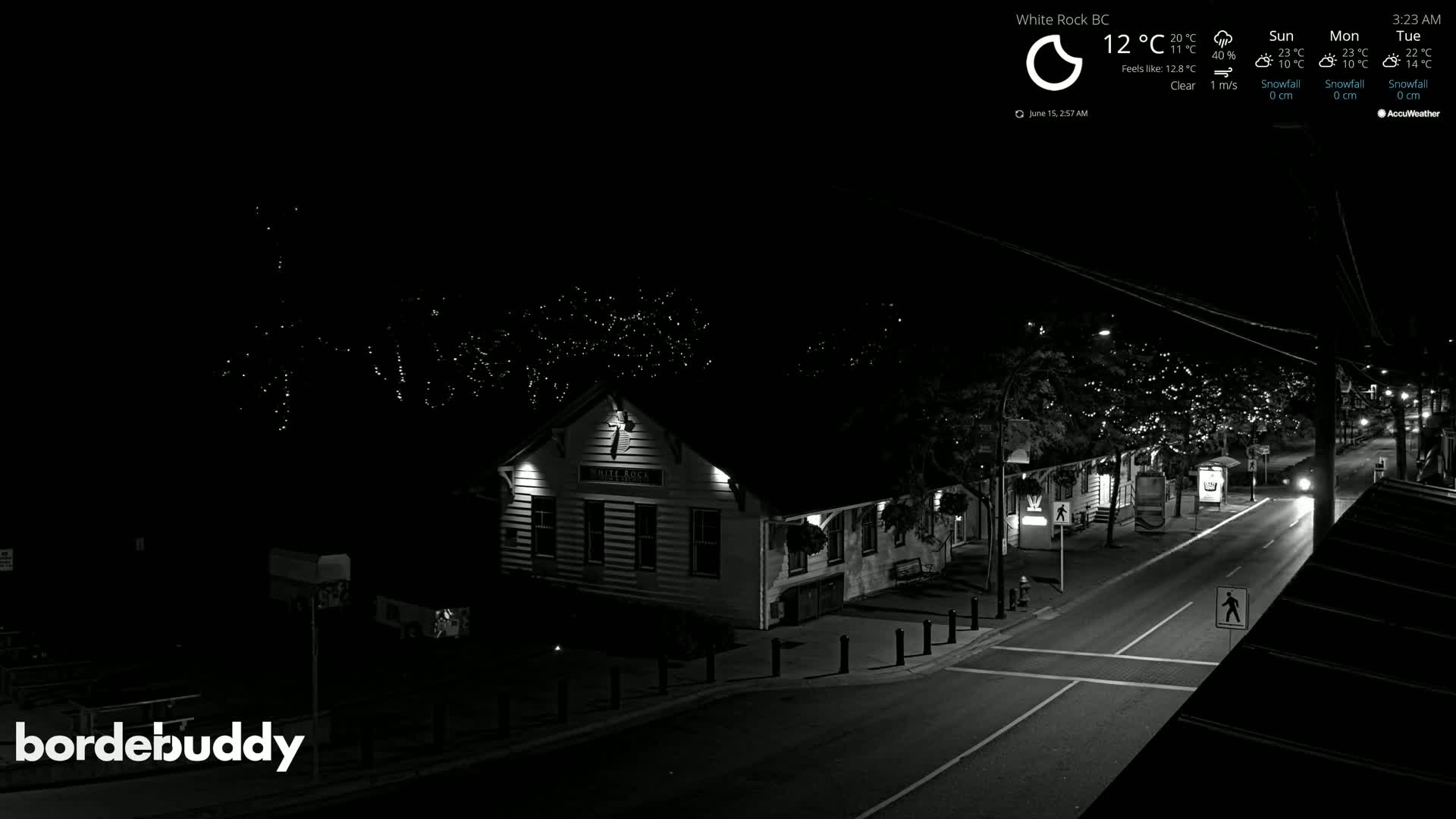 A nighttime, clear-weather view of a street scene shows a building lit up with string lights in the trees lining the street.