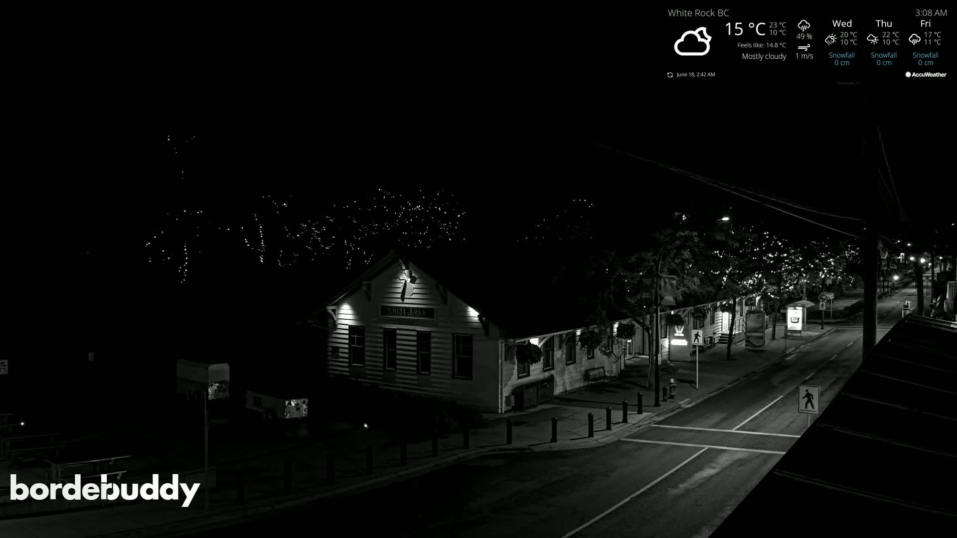 A mostly cloudy night scene shows a street with a building lit up by lights, under a dark sky.
