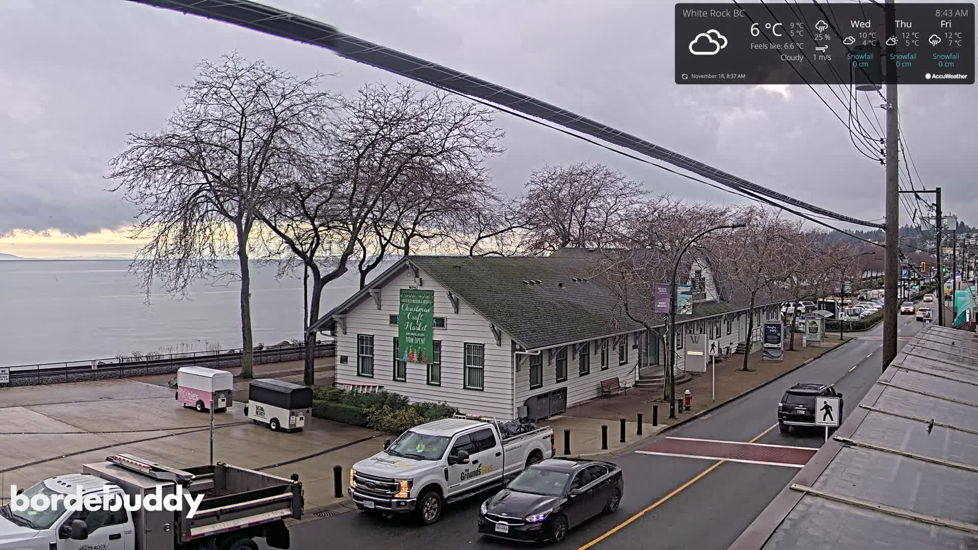 A mostly cloudy night scene shows a street with a building illuminated, some pedestrians, and string lights in the trees.
