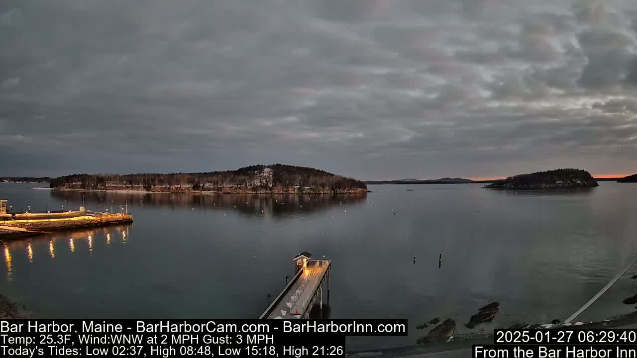Here is a description of the image: A long pier extends into a calm body of water at dawn under a mostly cloudy sky, with snow-dusted islands visible in the distance.