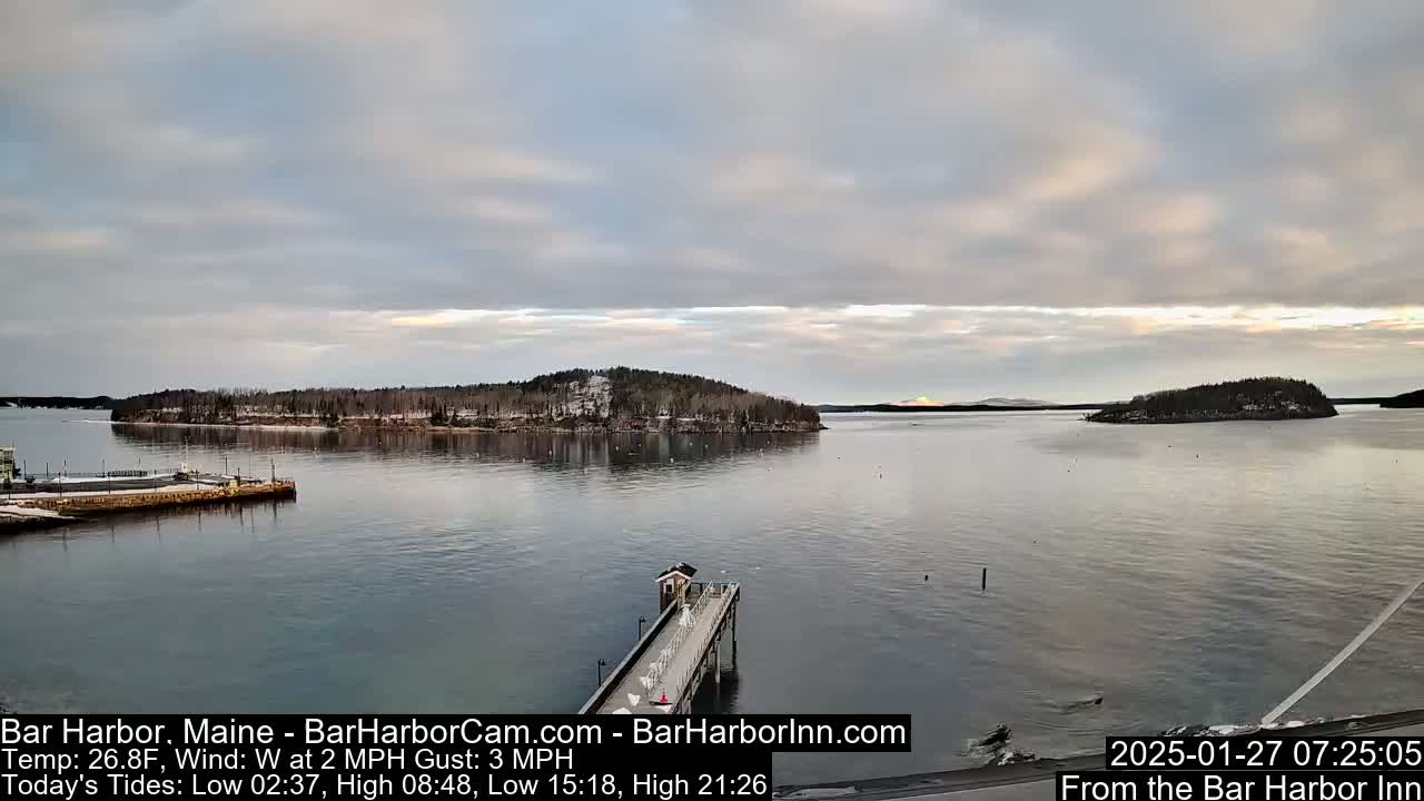 A long pier extends into a calm bay under a partly cloudy sky, with snow-dusted islands visible in the distance.