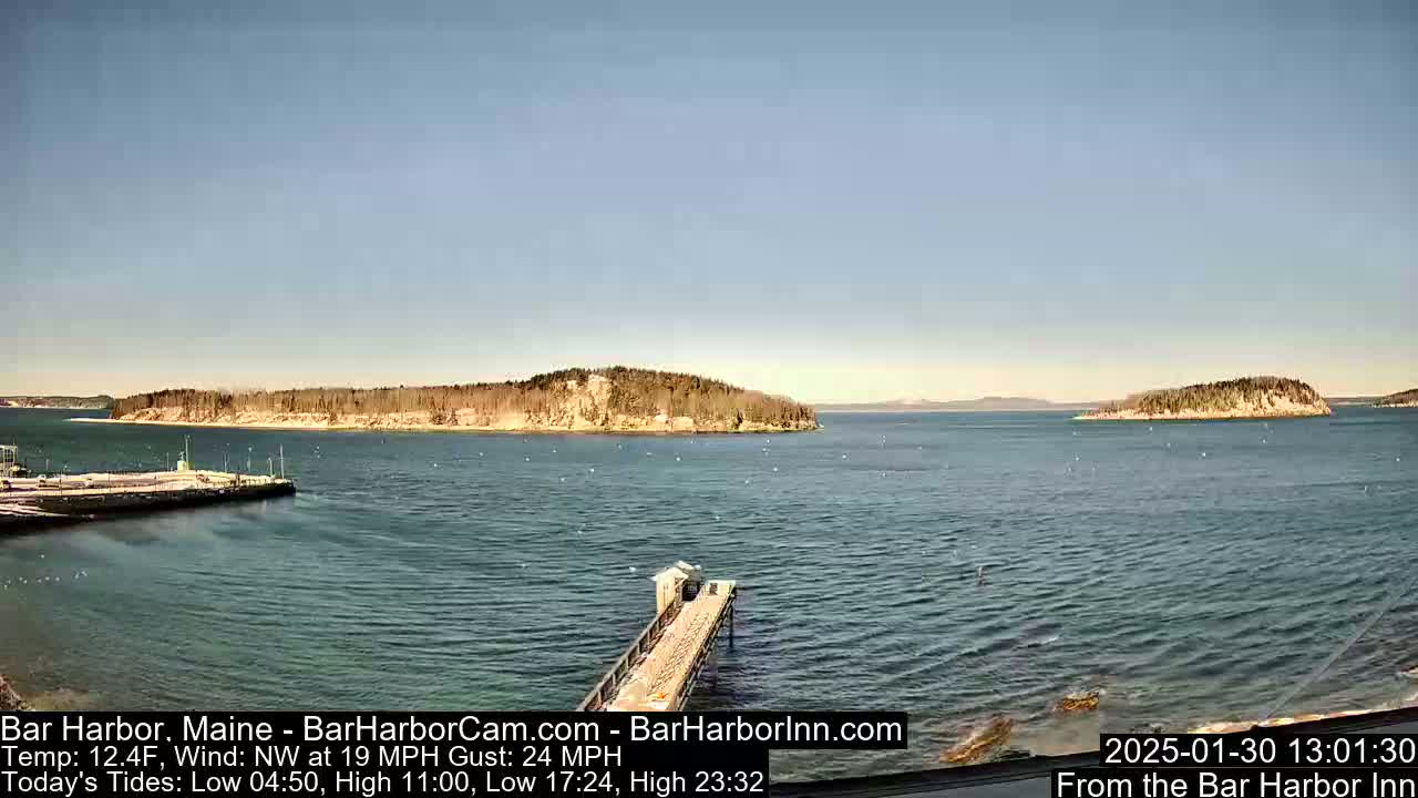 A long pier extends into a calm, blue body of water, with several small, tree-covered islands visible in the distance under a clear, bright sky.