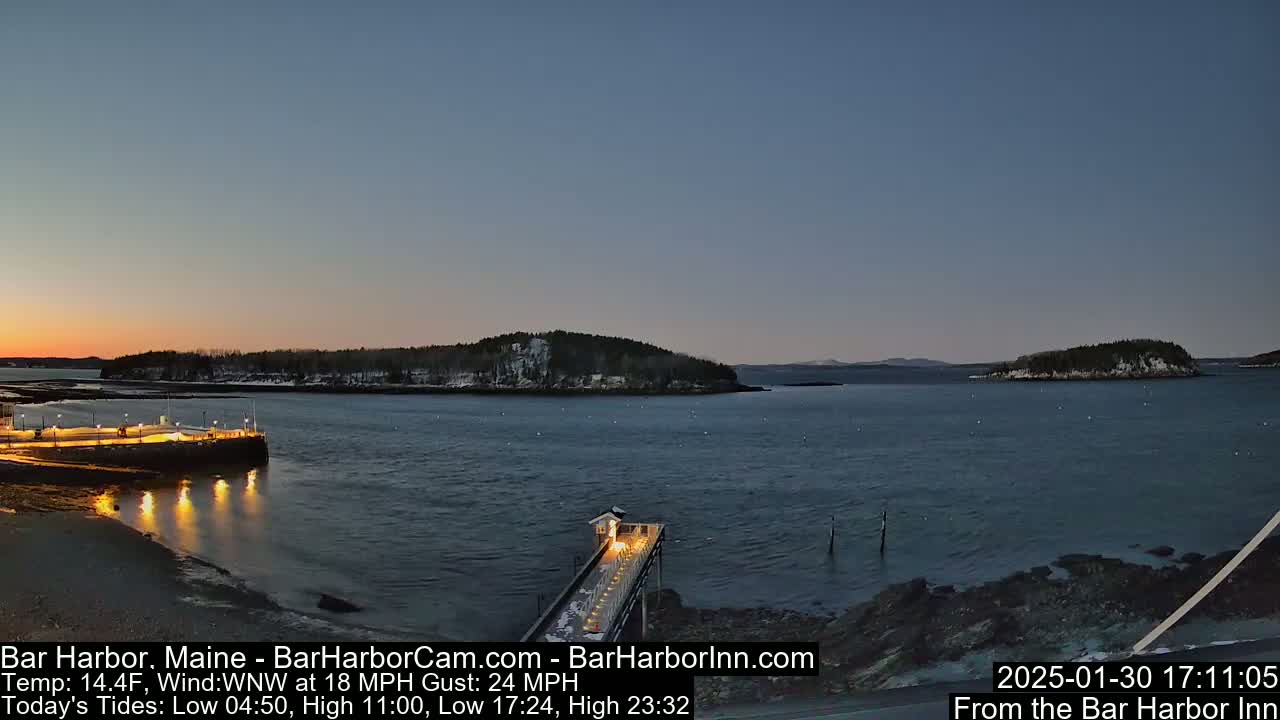 A twilight view of a snow-dusted harbor with a pier extending into calm water, under a mostly clear sky.