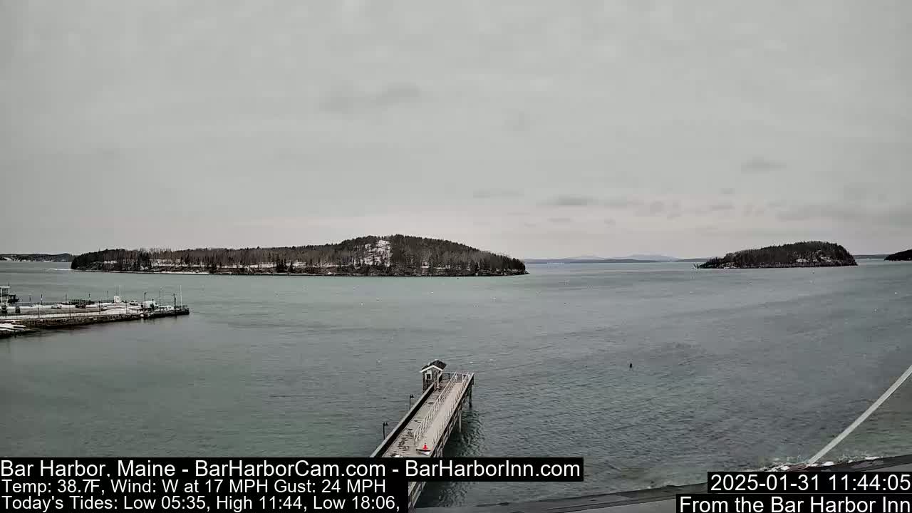 A long pier extends into a calm, gray body of water toward two small, snow-dusted islands under an overcast sky.