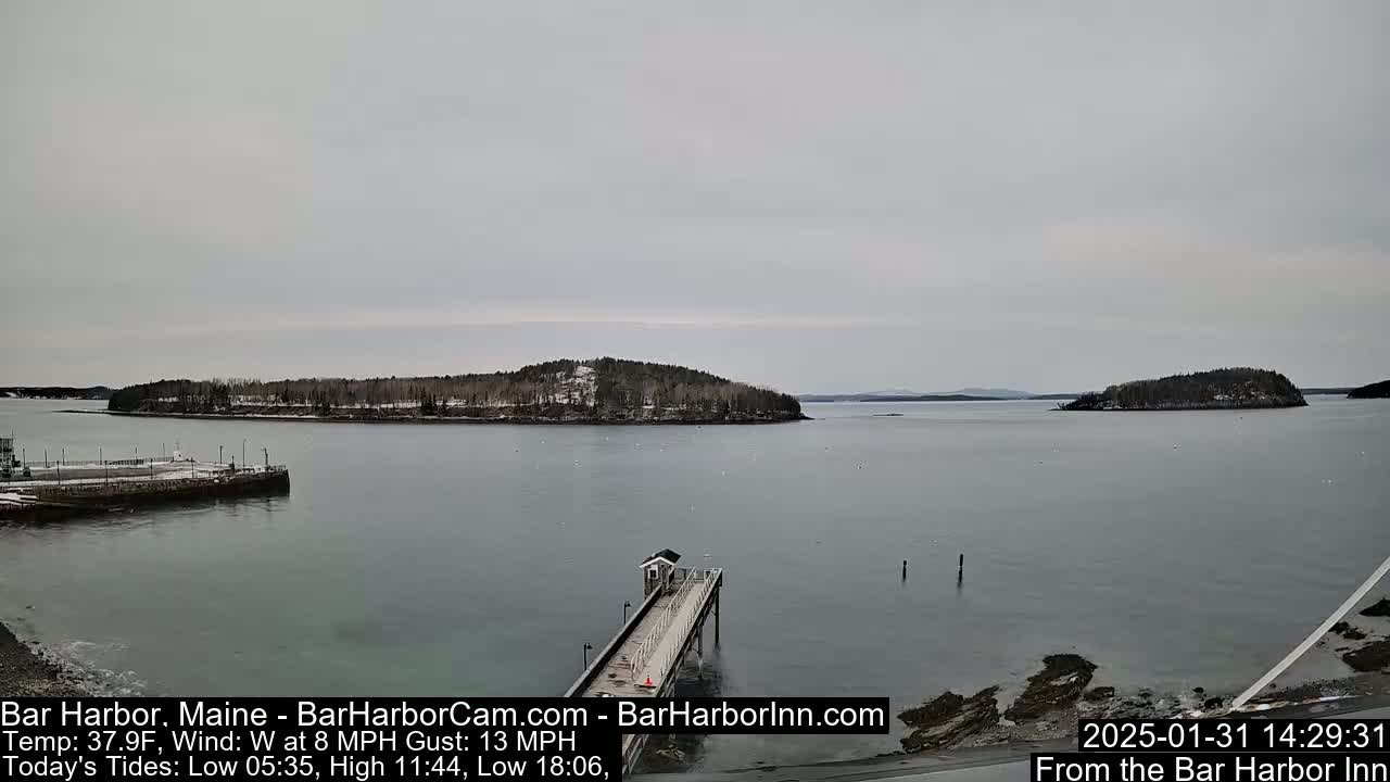 A long pier extends into a calm, gray body of water, with snow-dusted islands in the distance under an overcast sky.