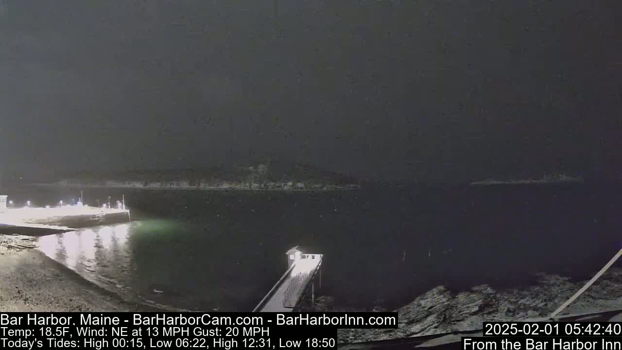 A nighttime view of a dark body of water with a pier extending from a shoreline, under a dark sky with a northeast wind.