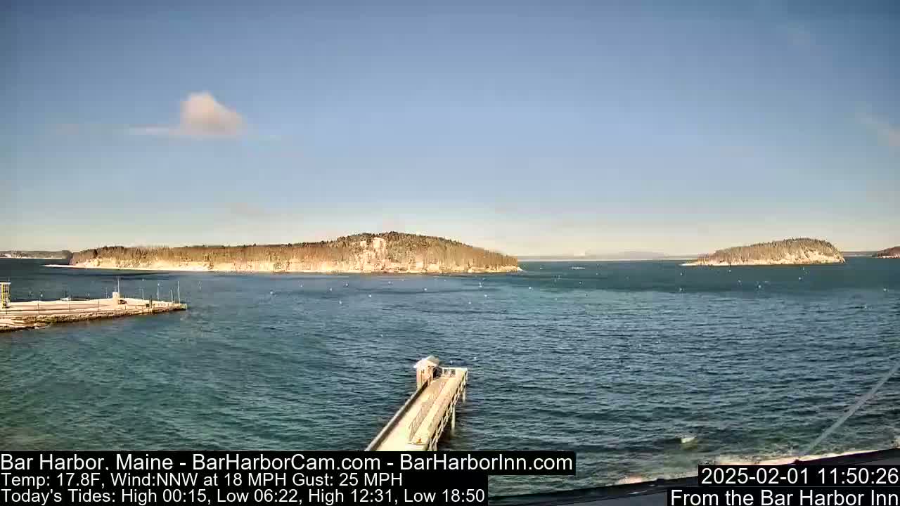 A mostly clear, sunny day shows a body of water with two small islands in the distance, a long pier extending from a shoreline, and a small building at the end of the pier.