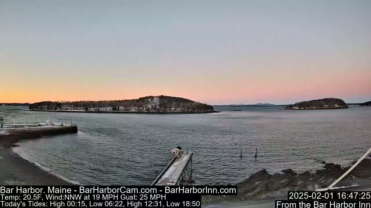 A calm harbor at sunset with two snow-dusted islands in the distance, under a pale pink sky.