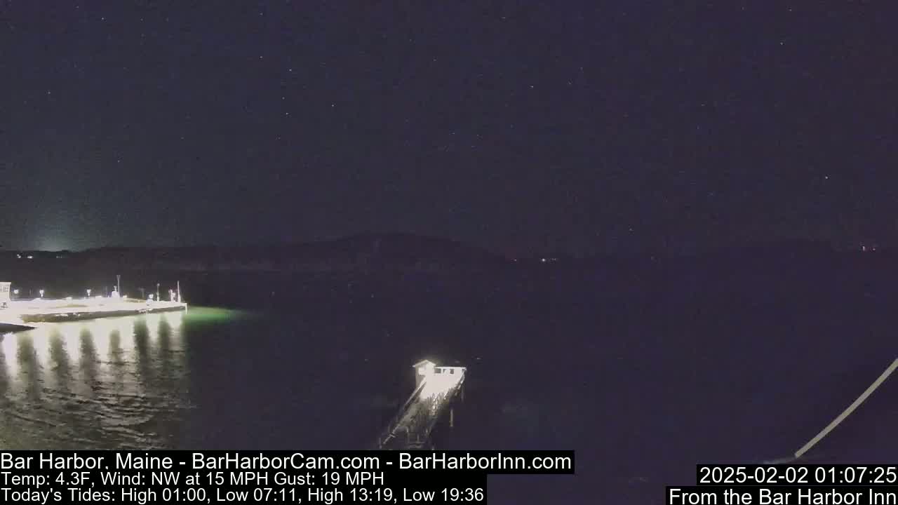 A nighttime, long shot of a lit-up pier extending into a dark body of water under a starry sky with a northwest wind.