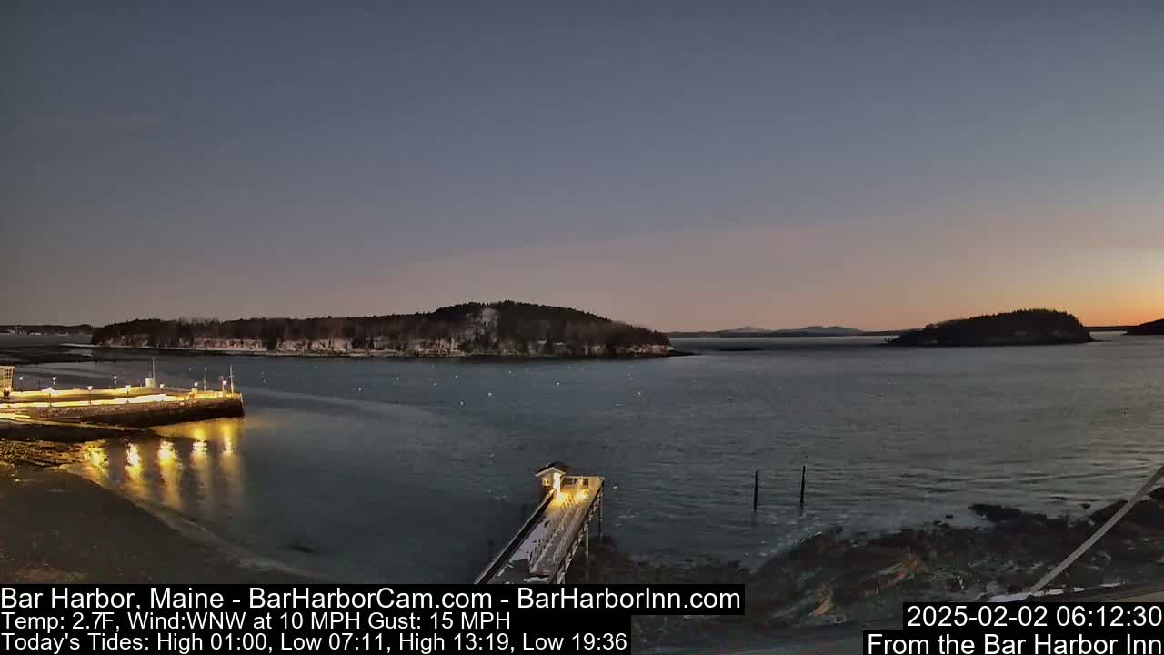 A twilight view of a harbor, with a pier extending into calm water,  surrounded by snow-dusted islands under a clear sky.