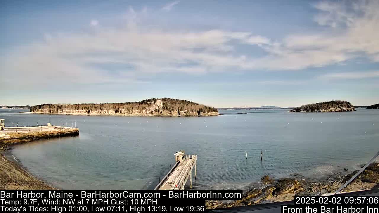A calm, partly cloudy day shows a long pier extending into a bay with several small islands in the distance.
