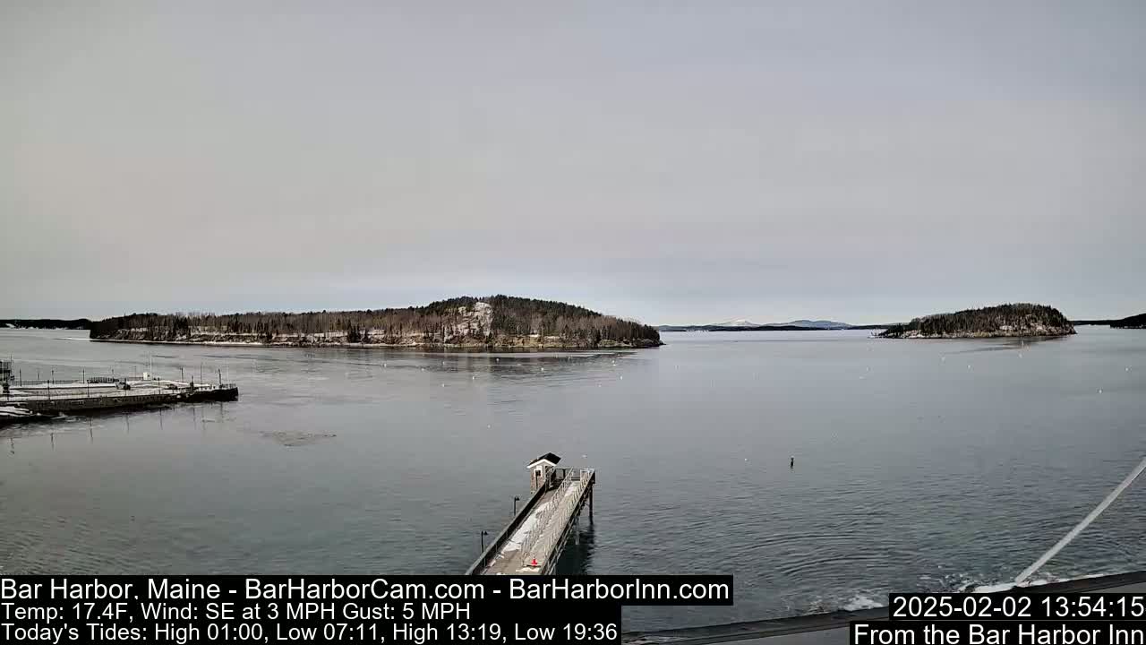 A calm, overcast day shows a view of a snow-dusted island and a long pier extending into a gray body of water.