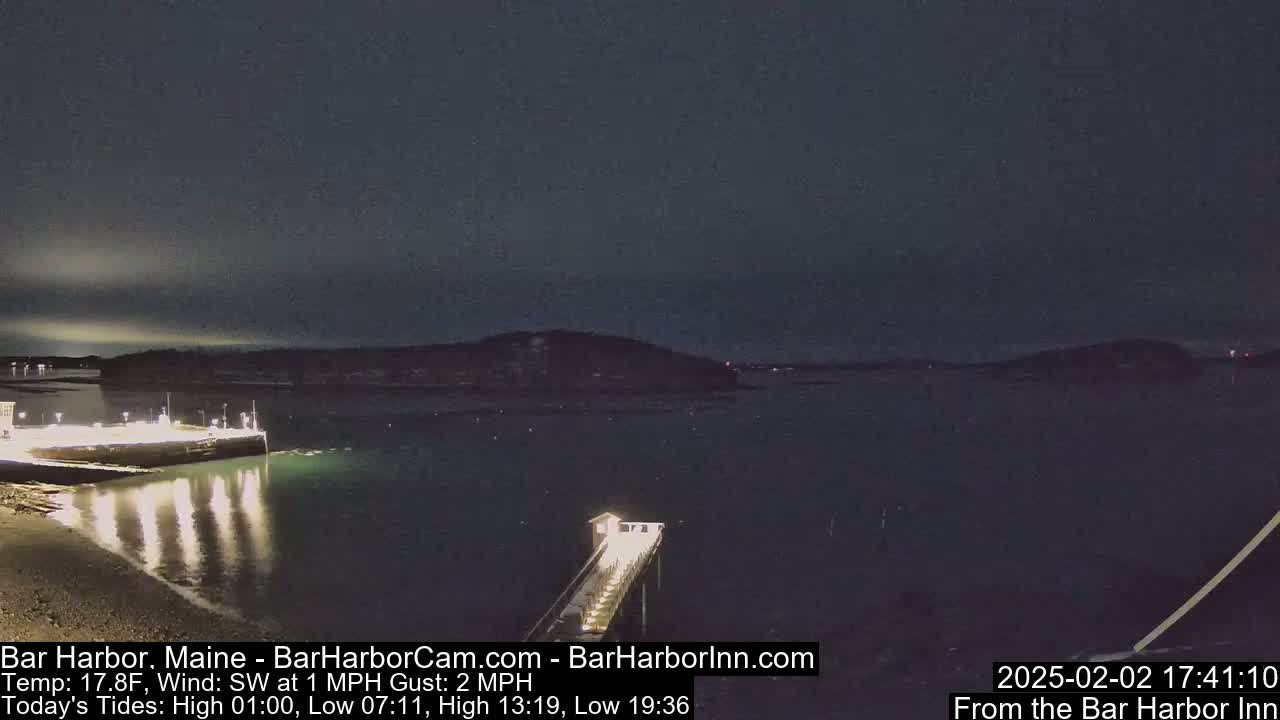 A nighttime view of a calm harbor with a pier extending into the water under a dark sky.