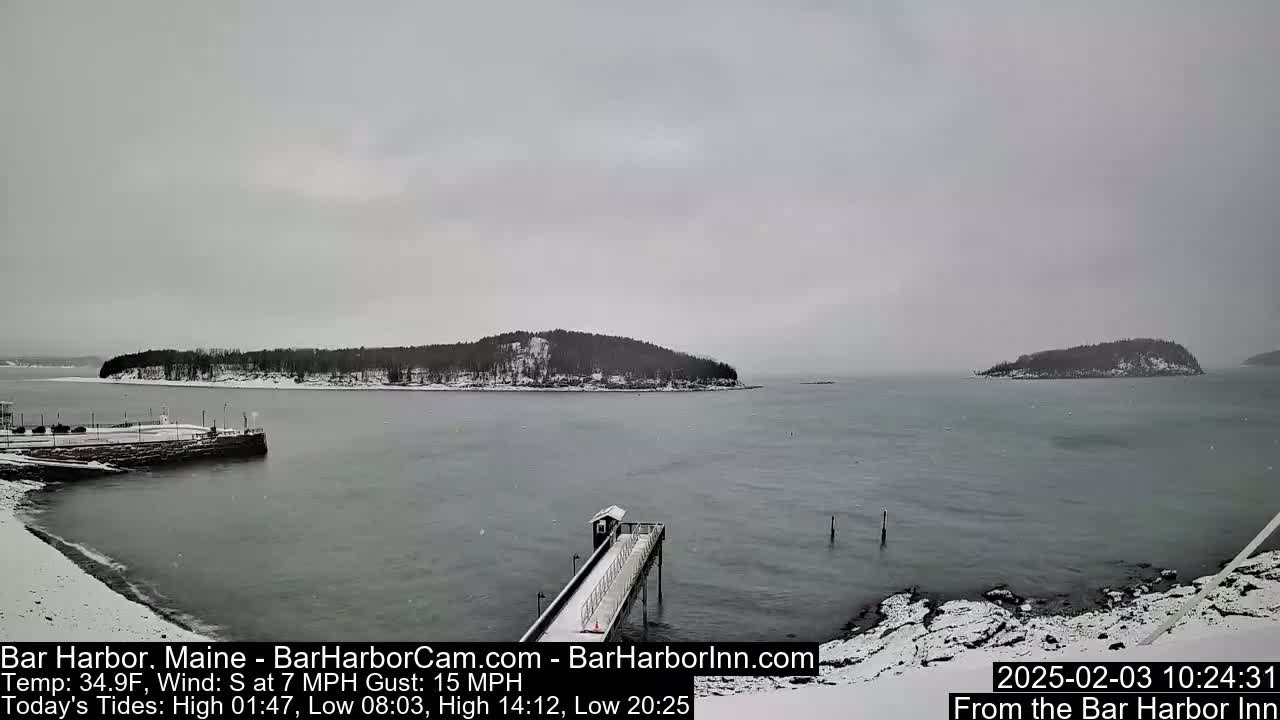 A snow-covered pier extends into a calm bay, with snow-dusted islands in the distance under an overcast sky.