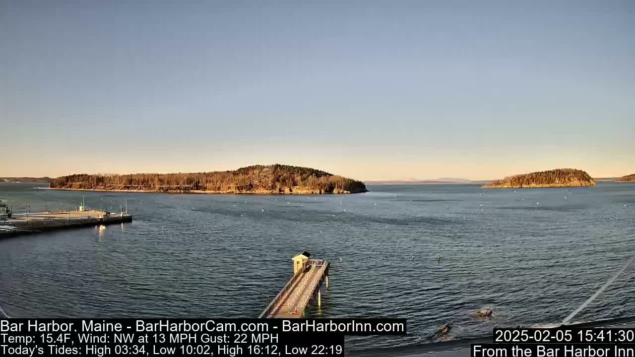 A calm harbor scene shows two small, tree-covered islands in the distance under a clear, pale blue sky.