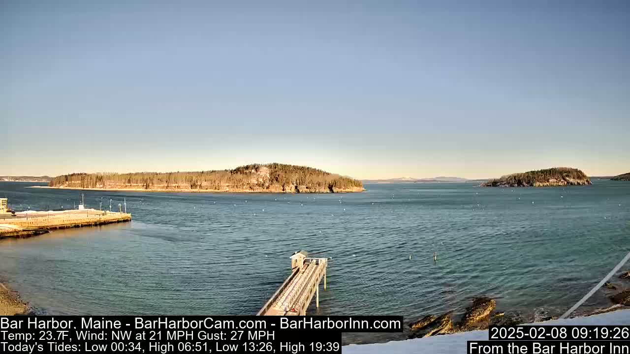 A partly sunny day shows a harbor with a long pier extending into the water, two islands in the distance, and some snow on the ground.