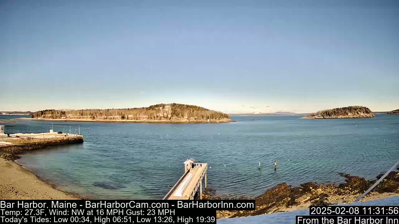 A calm harbor with a long pier extending into the water, surrounded by islands and a clear blue sky under sunny conditions.