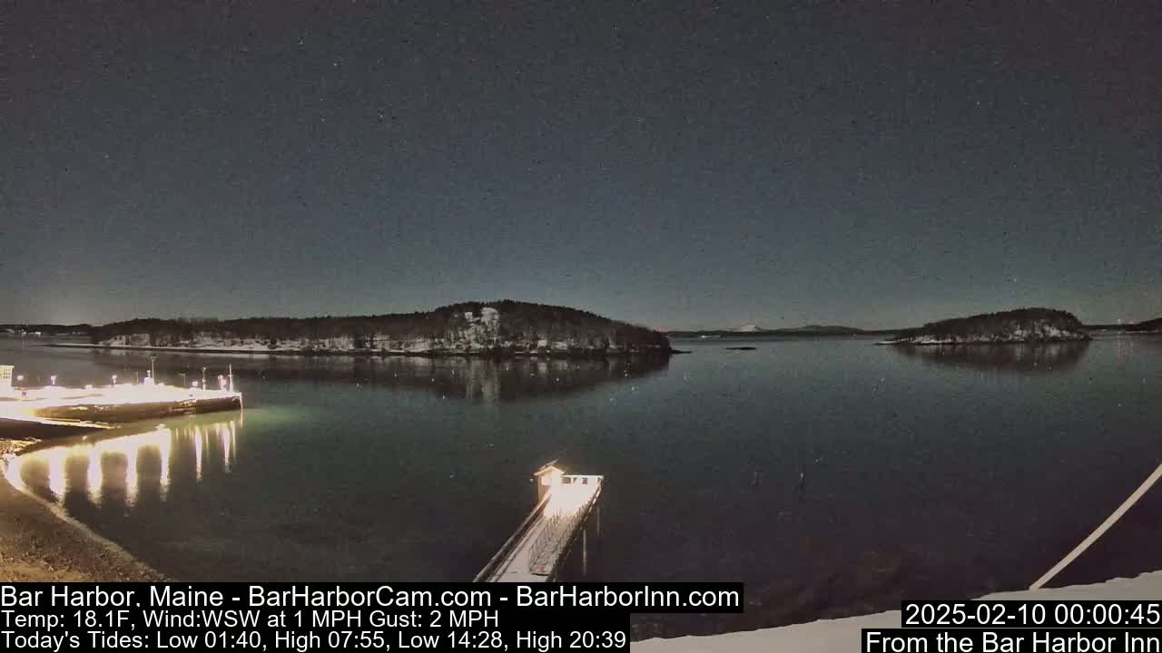 A nighttime view of a snow-covered harbor with a lit pier extending into calm, dark water, under a clear, starry sky.