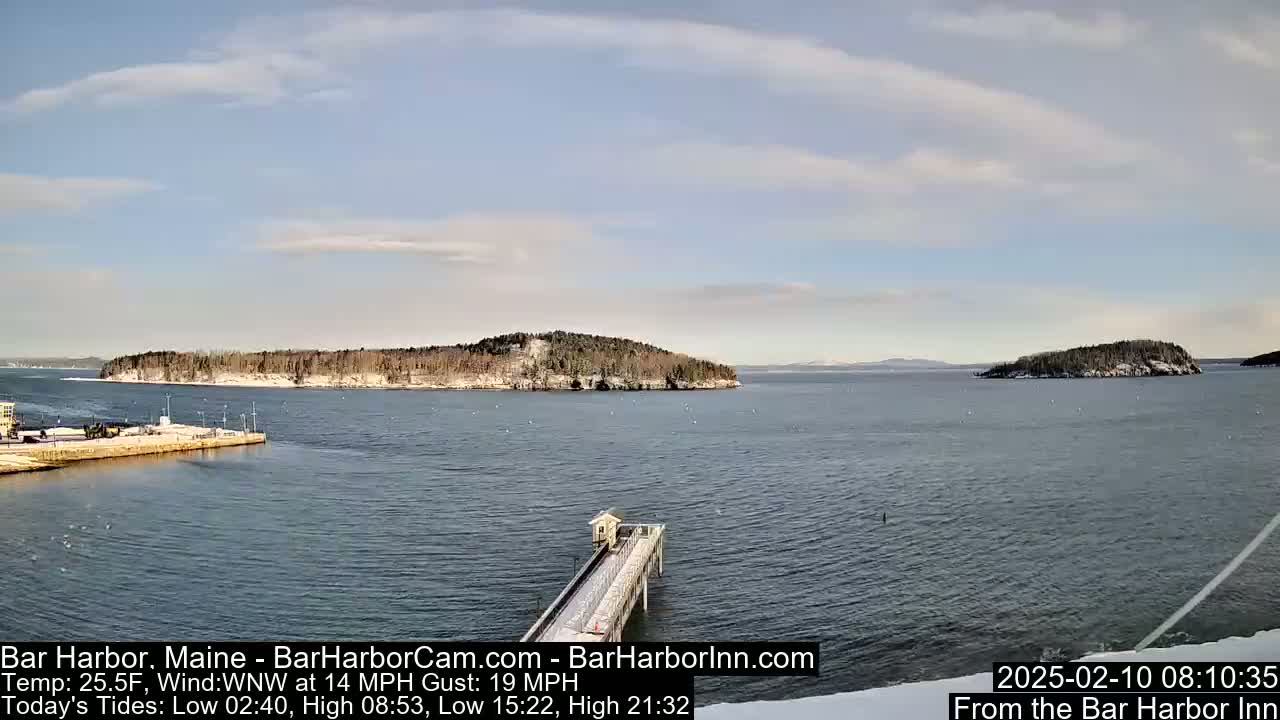 A long pier extends into a calm body of water, with snow-dusted islands visible in the distance under a partly cloudy sky.