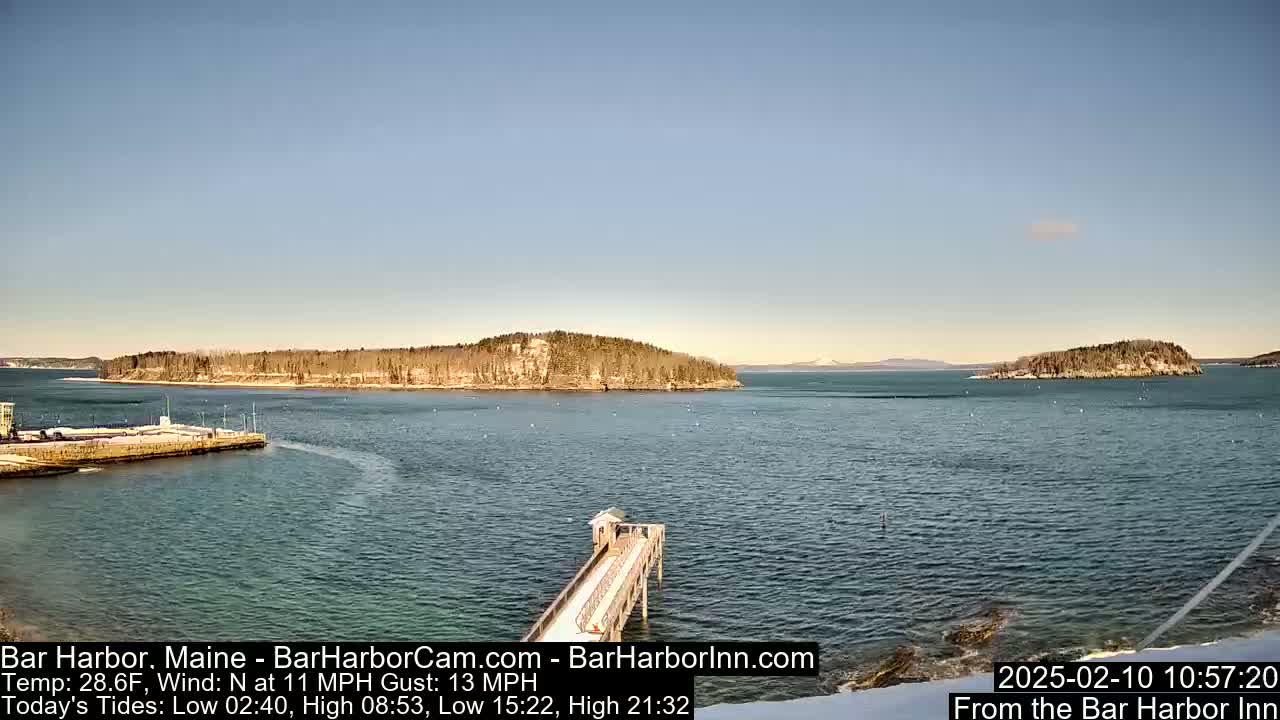 A long pier extends into a calm body of water under a clear blue sky, with snow-covered islands in the distance.