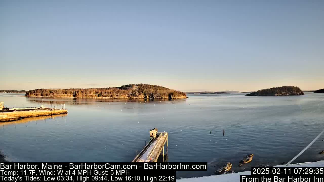 A long pier extends into a calm bay under a clear, light blue sky, with islands in the background.