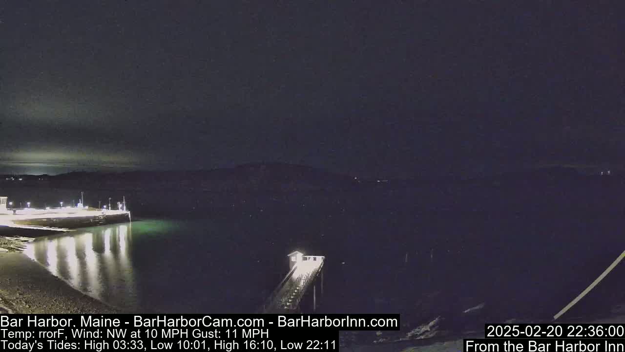 A nighttime view of a calm harbor with a pier extending into the water under a dark sky, with a northwest wind at 10 mph and gusts up to 11 mph.