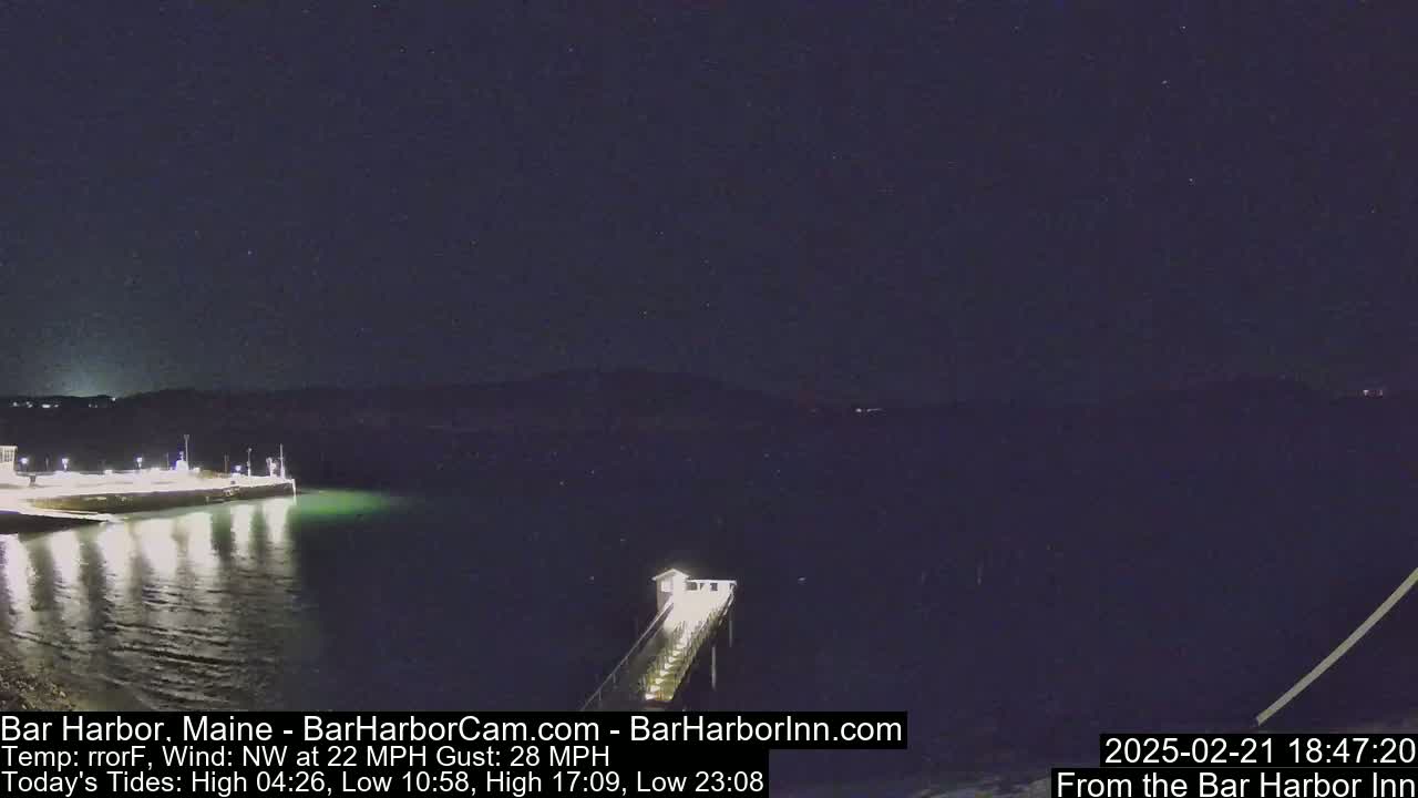 A nighttime view of a dark harbor with a pier extending into the water under a clear, dark sky, with a northwest wind blowing at 22 mph and gusts up to 28 mph.