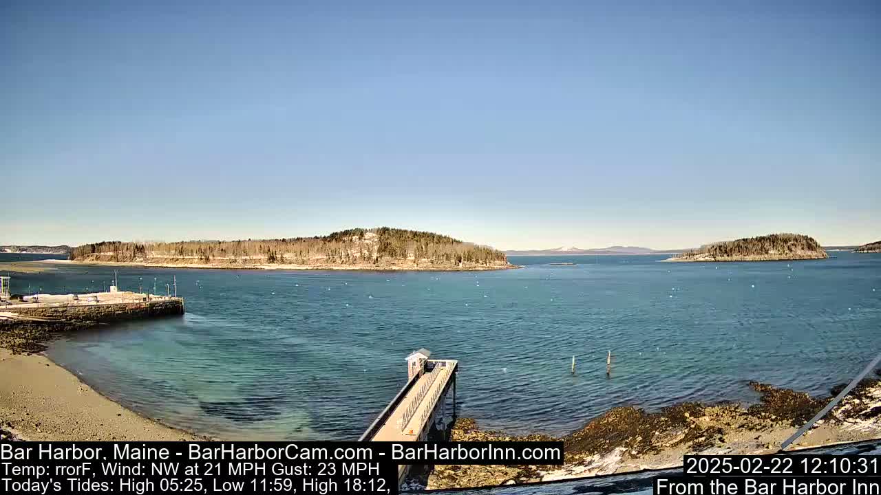 A calm, blue body of water stretches out to tree-covered islands under a clear, bright blue sky.