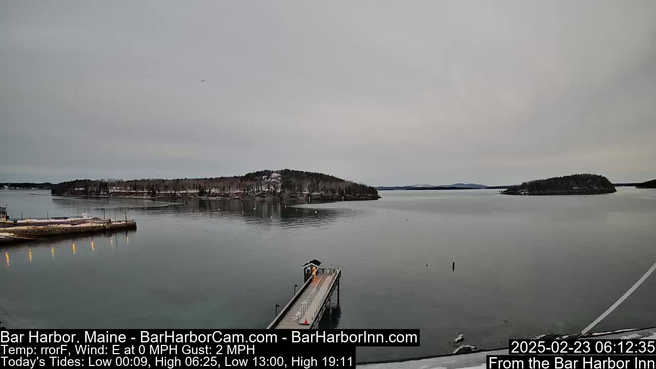 A long pier extends into a calm, gray body of water, with snow-covered islands visible in the distance under an overcast sky.