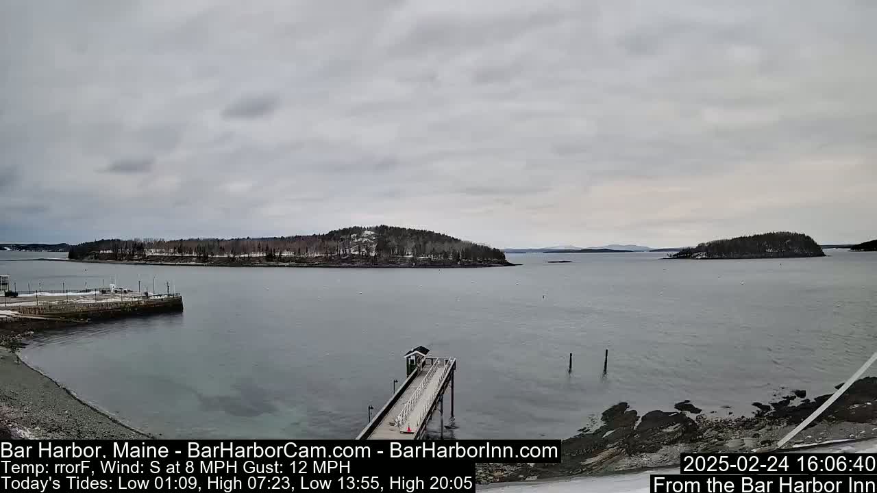 A long pier extends into a calm, gray-sky harbor, with snow-dusted islands in the distance.