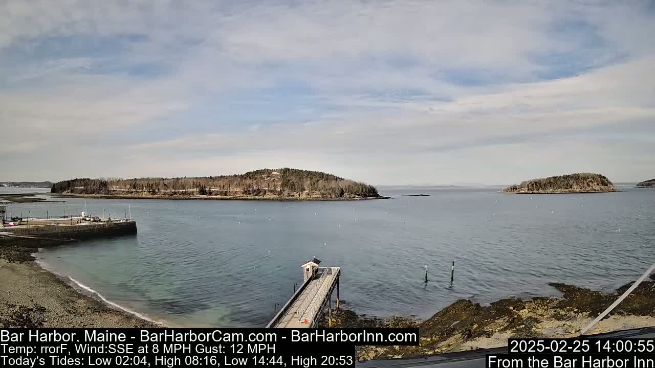 A long pier extends into a calm bay, with several small, tree-covered islands in the distance under a mostly cloudy sky.