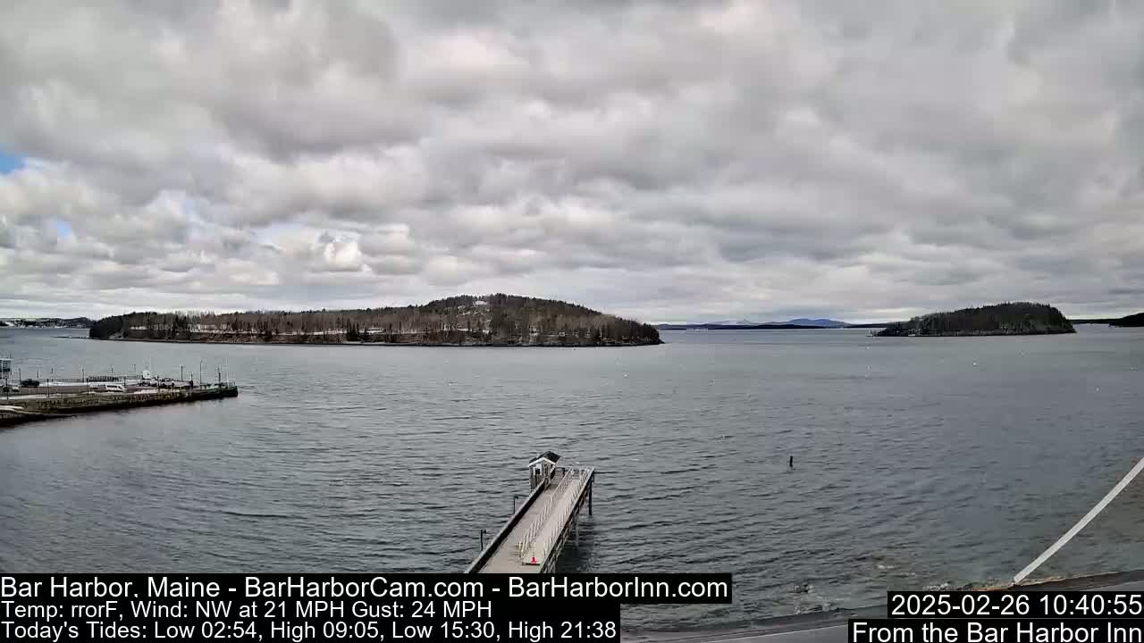 A long pier extends into a body of water under a cloudy sky, with islands and a distant mountain range visible in the background.