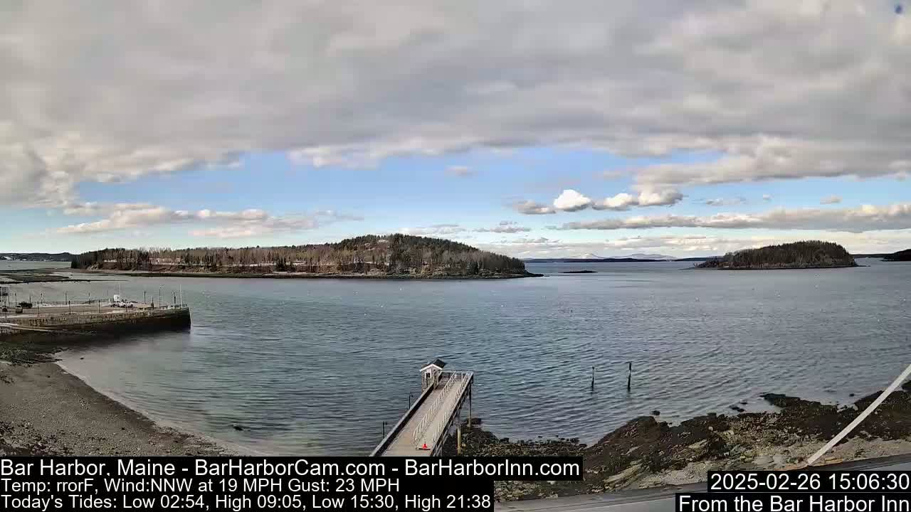 A partly cloudy day reveals a tranquil harbor scene with several small islands, a long pier extending into the water, and a rocky shoreline.