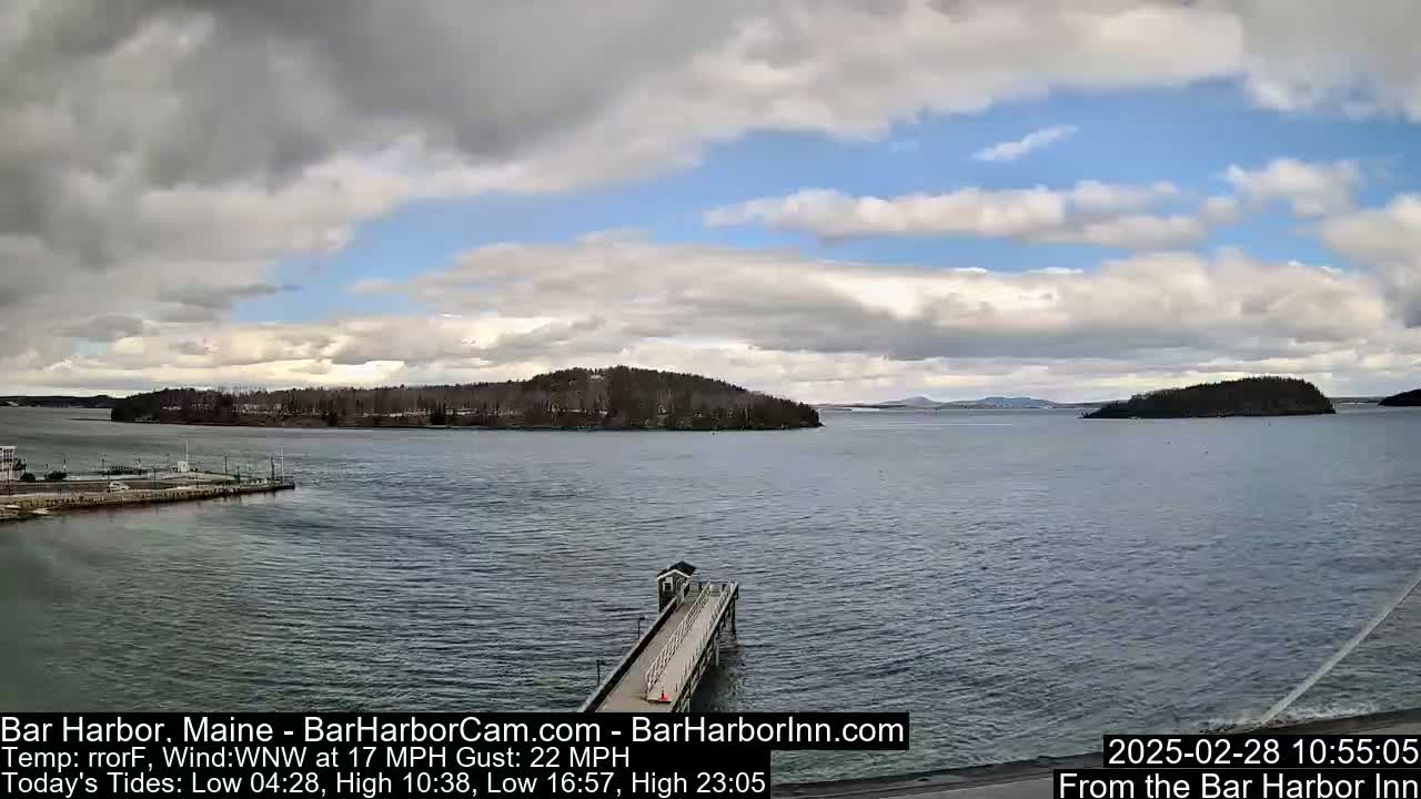 A partly cloudy day shows a tranquil body of water with islands in the distance and a long pier extending from a shoreline.