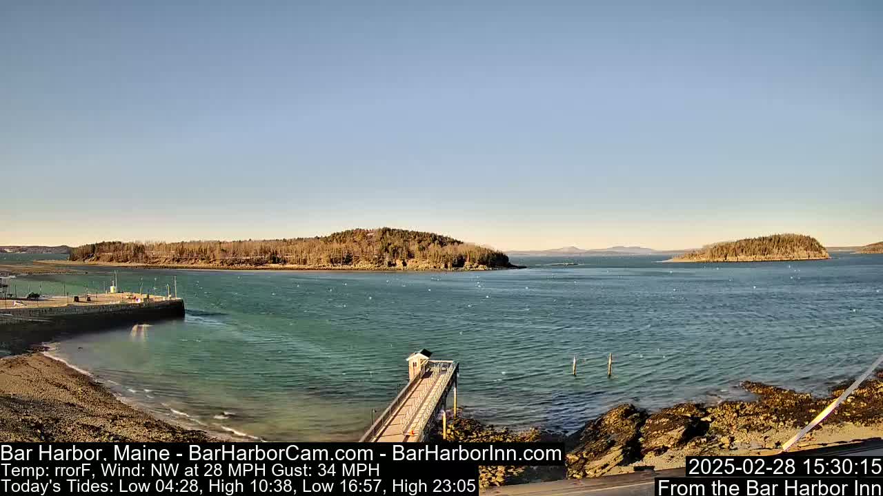 A harbor with a long pier extending into the water, under a clear blue sky, with islands in the distance and a northwest wind.