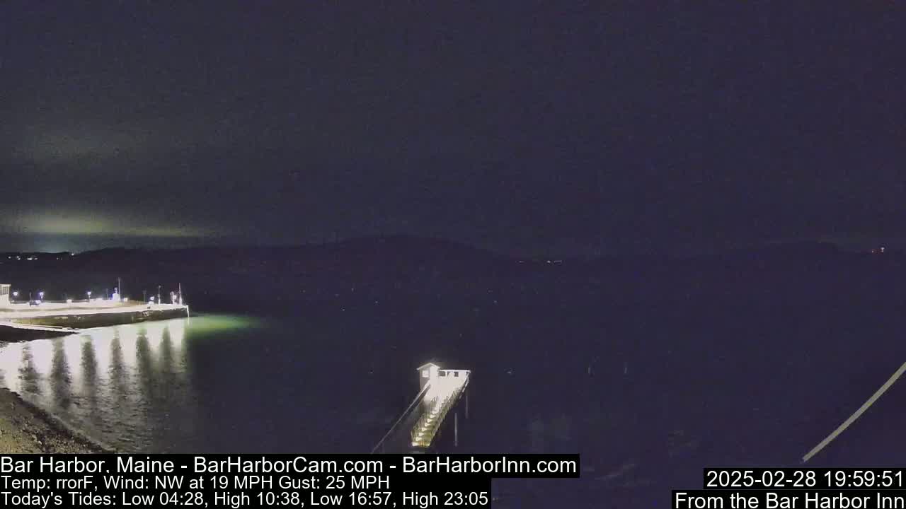A nighttime view of a calm harbor with a long pier extending into the water under a dark sky, with a northwest wind blowing at 19 mph and gusts up to 25 mph.