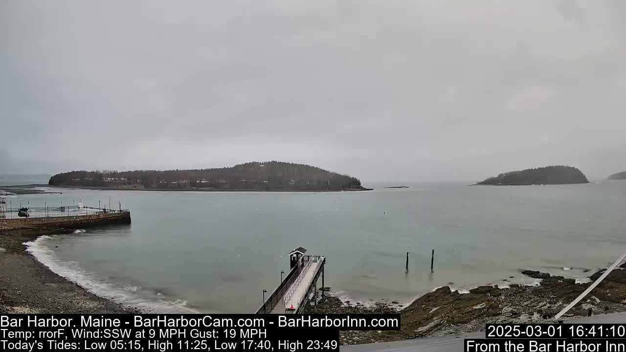 A long pier extends into a calm, gray body of water under an overcast sky, with small islands in the distance.