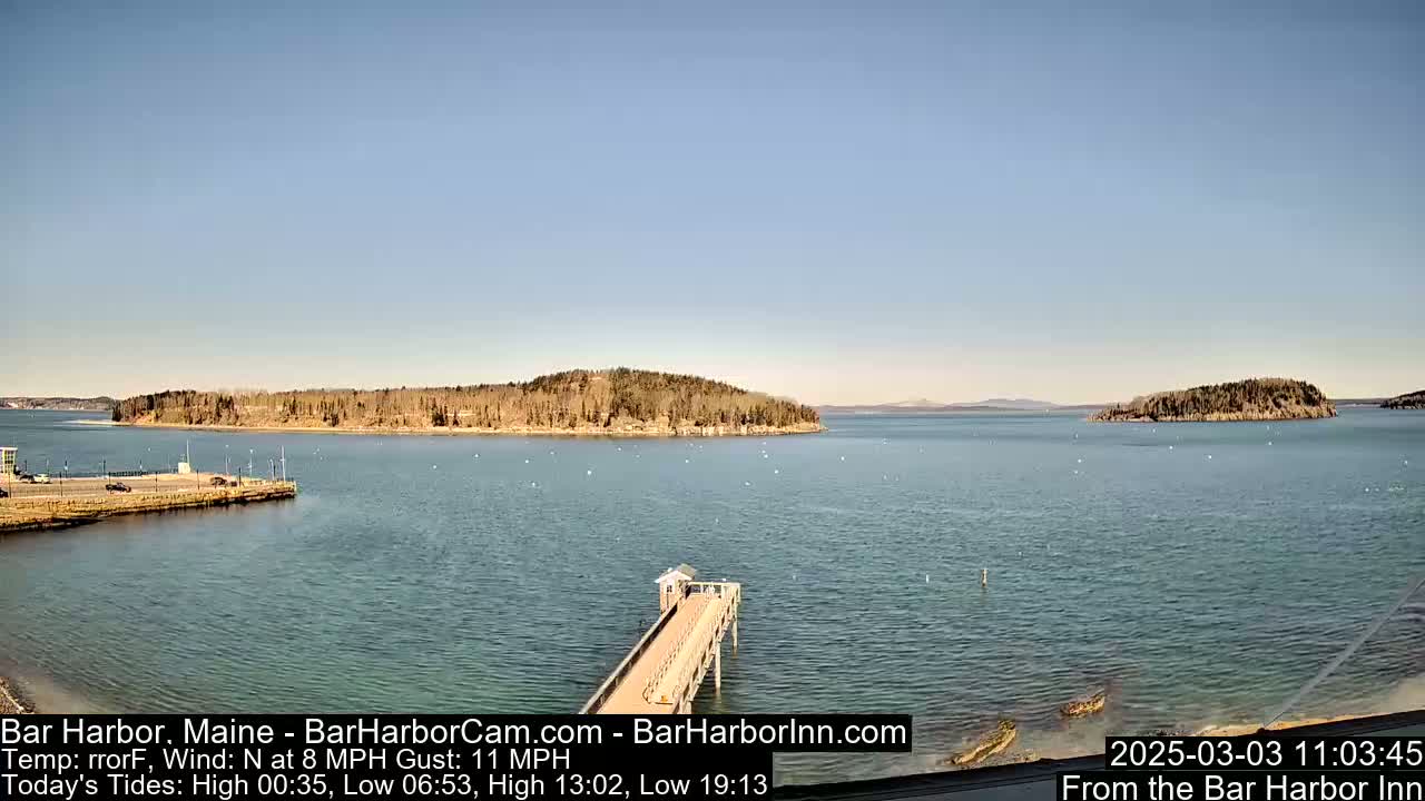 A calm harbor scene on a clear day shows a long pier extending into the water, with several islands visible in the distance.