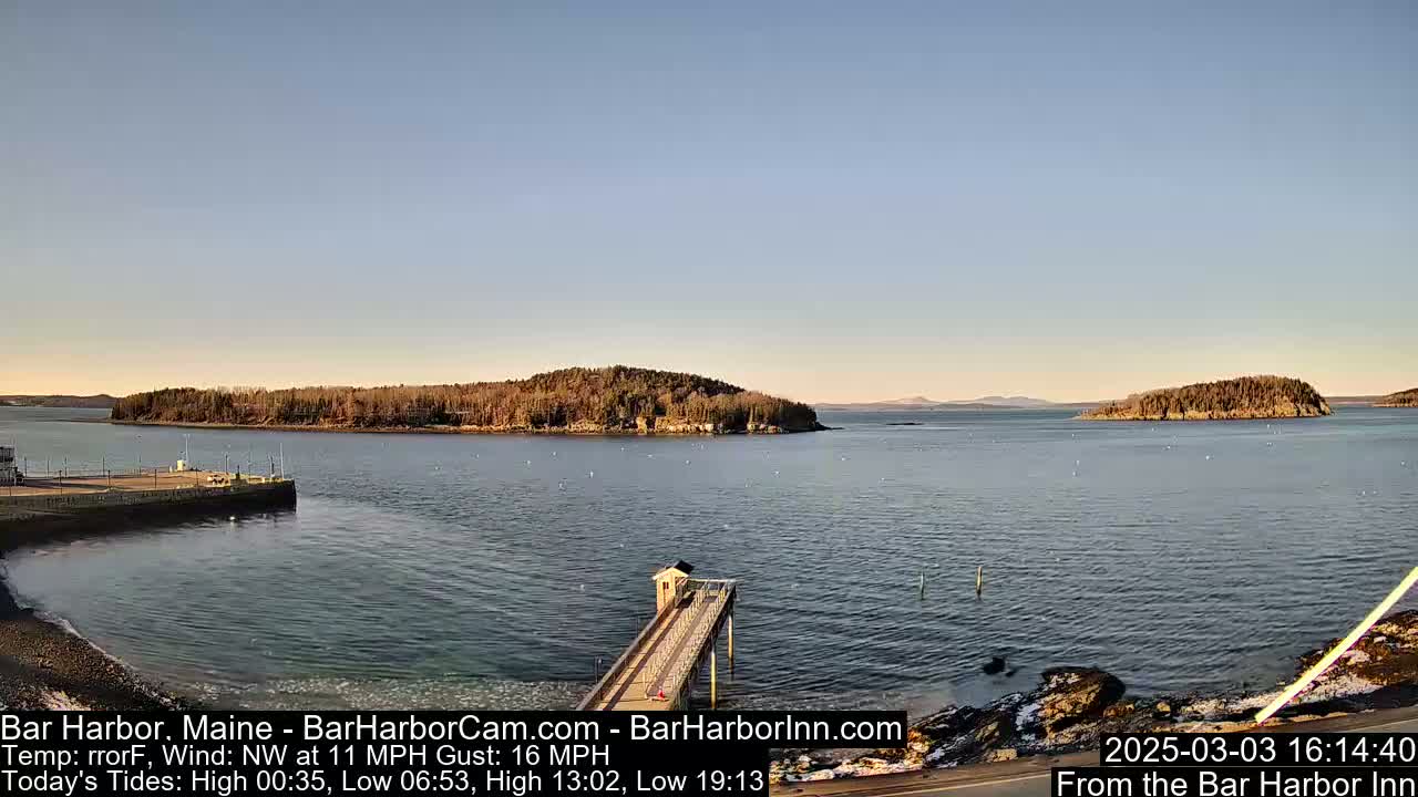 A calm harbor scene with a long pier extending into the water, under a clear, light-blue sky, shows several small islands in the distance.