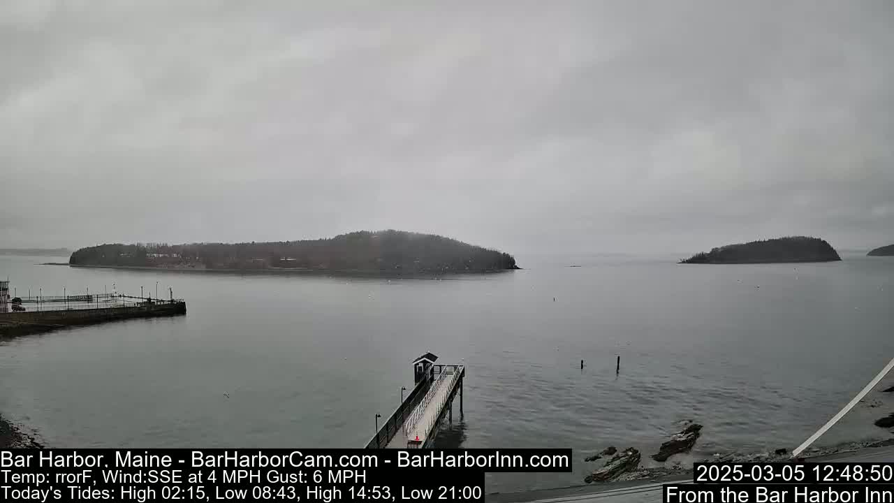 A long pier extends into a calm, gray body of water under an overcast sky, with several small islands in the distance.