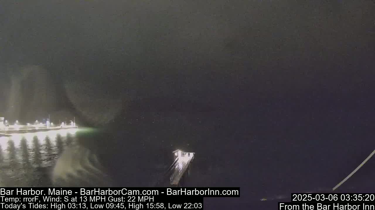 A nighttime, dark scene shows a pier extending into a choppy body of water under a cloudy sky, with a south wind at 13 mph and gusts up to 22 mph.