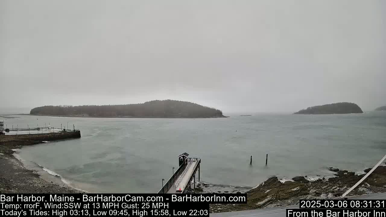 A gray, overcast day shows a harbor scene with a long pier extending into the water,  two small islands in the distance, and a rocky shoreline.