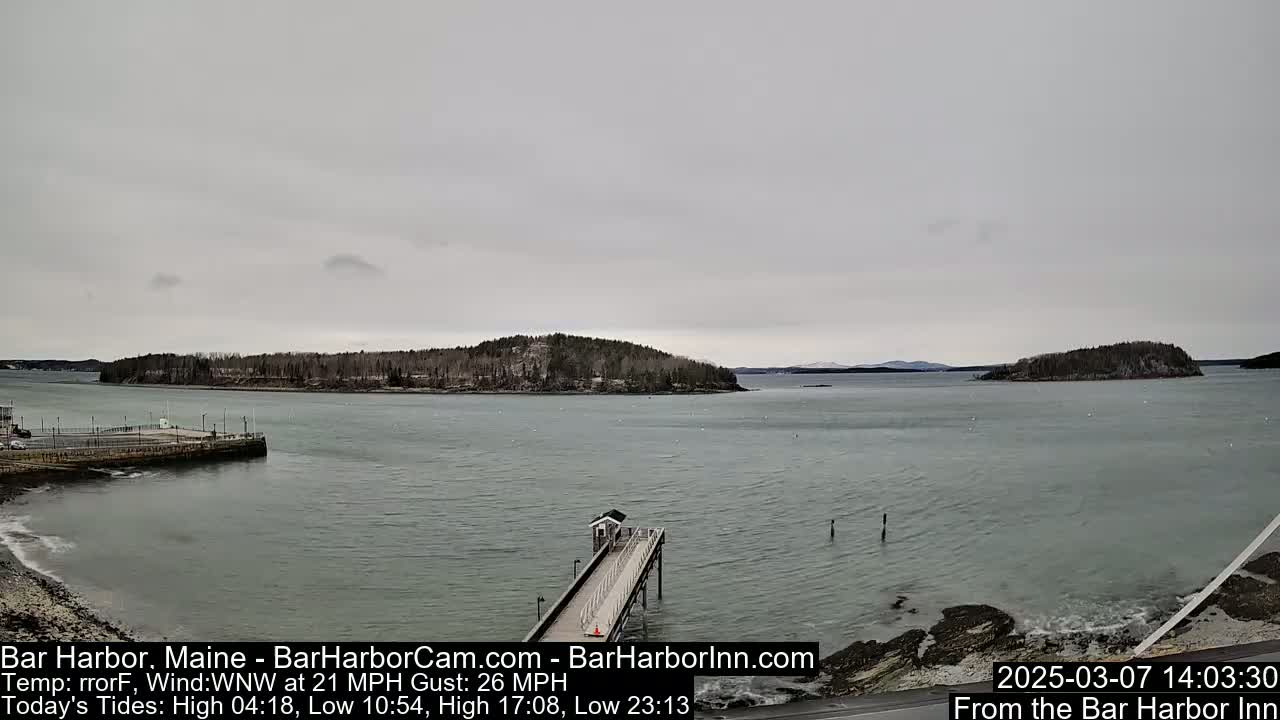 A long pier extends into a calm body of water under an overcast sky, with several islands visible in the distance.