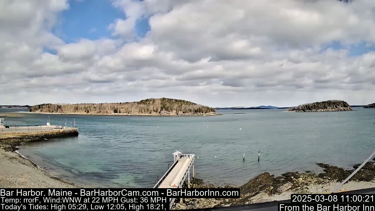 A partly cloudy day reveals a tranquil body of water with small islands and a pier extending into the calm sea.