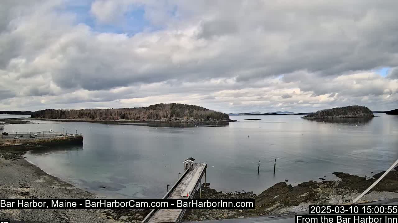 A calm bay with several small islands under a partly cloudy sky is viewed from a pier.