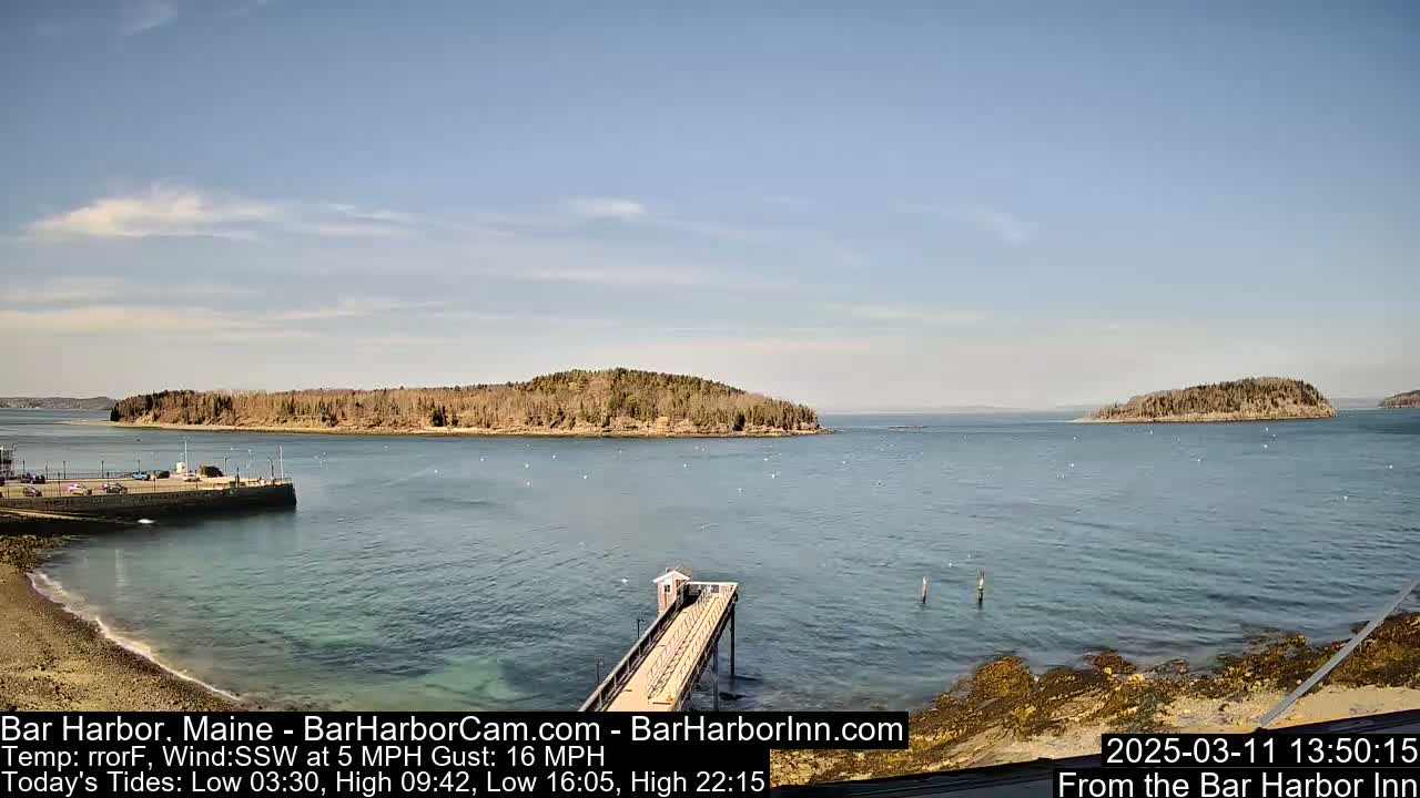 A calm body of water with two small, tree-covered islands in the distance, under a mostly clear sky, is viewed from a pier.