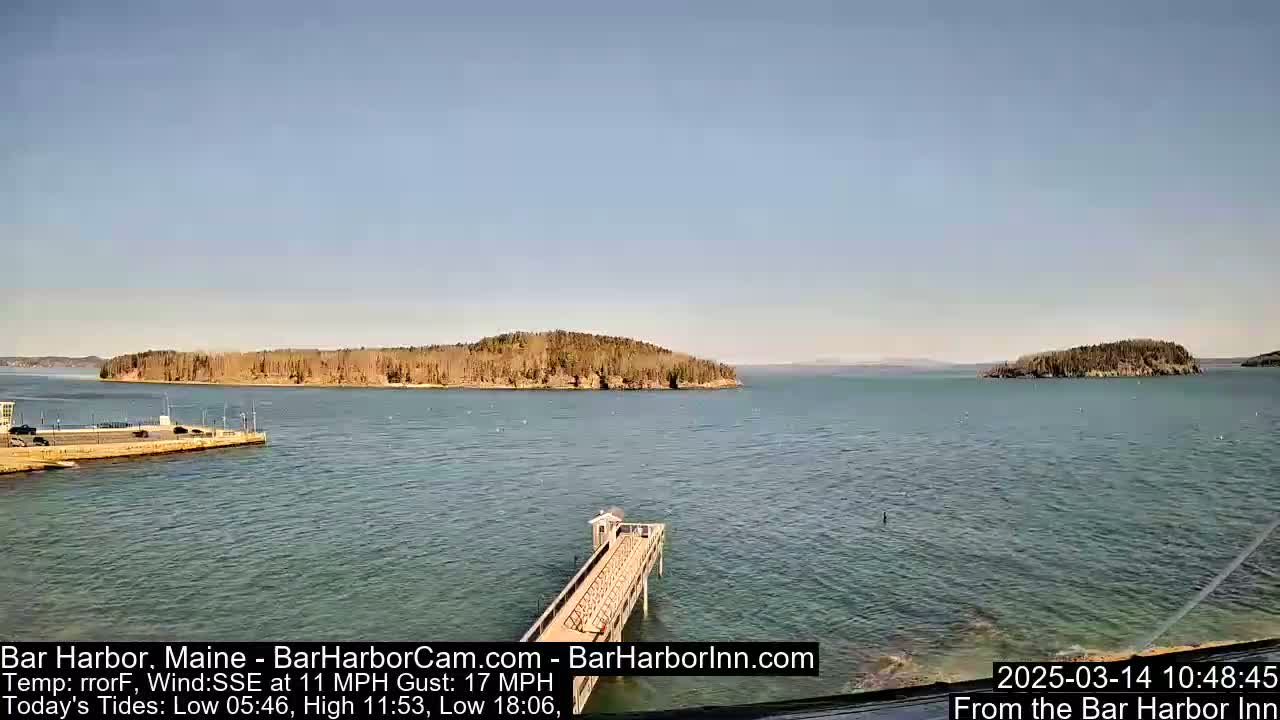 A calm, sunny day shows a tranquil body of water with a long pier extending from a land mass into the water, with islands in the distance.